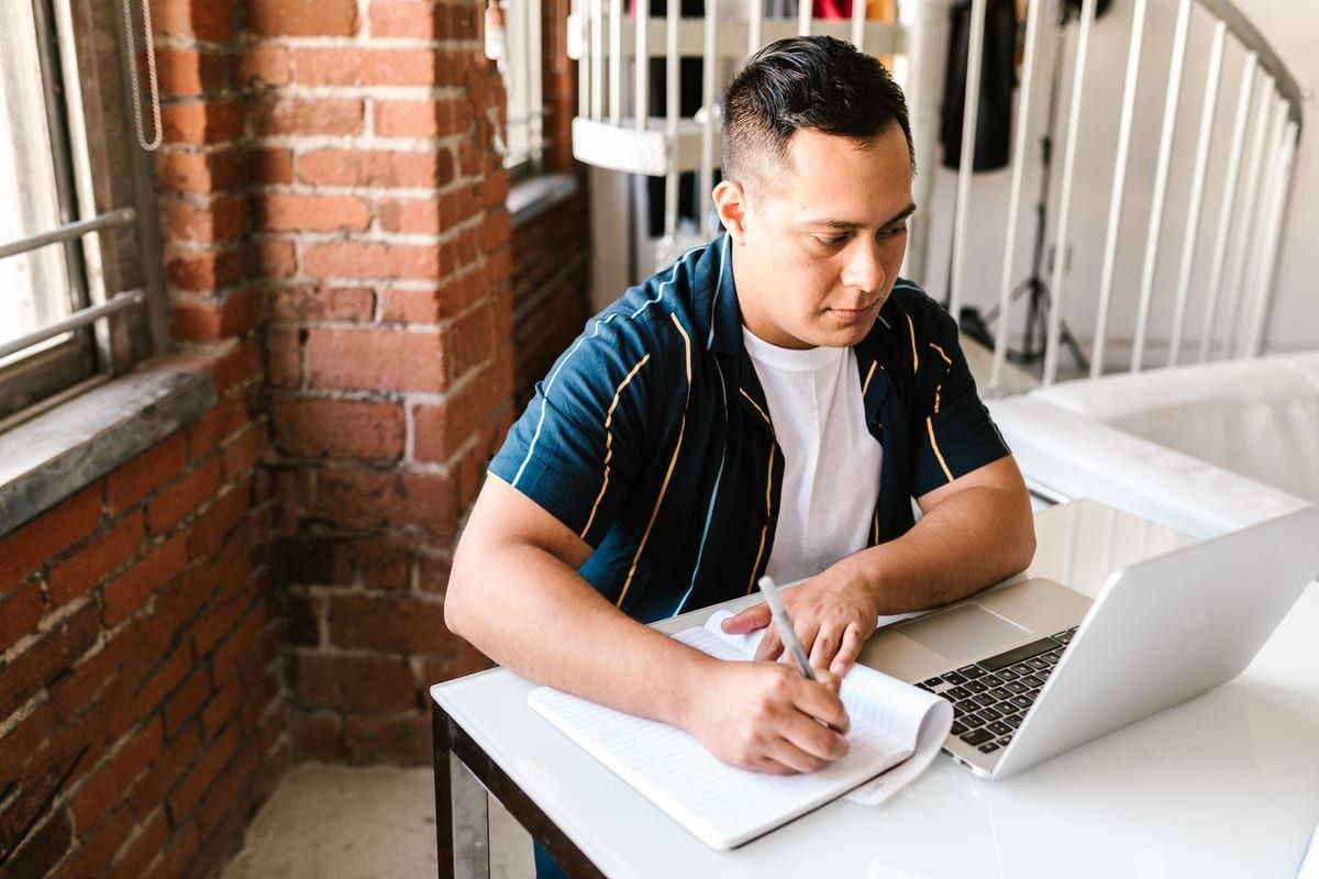 A learner working through a lesson with a notebook and laptop